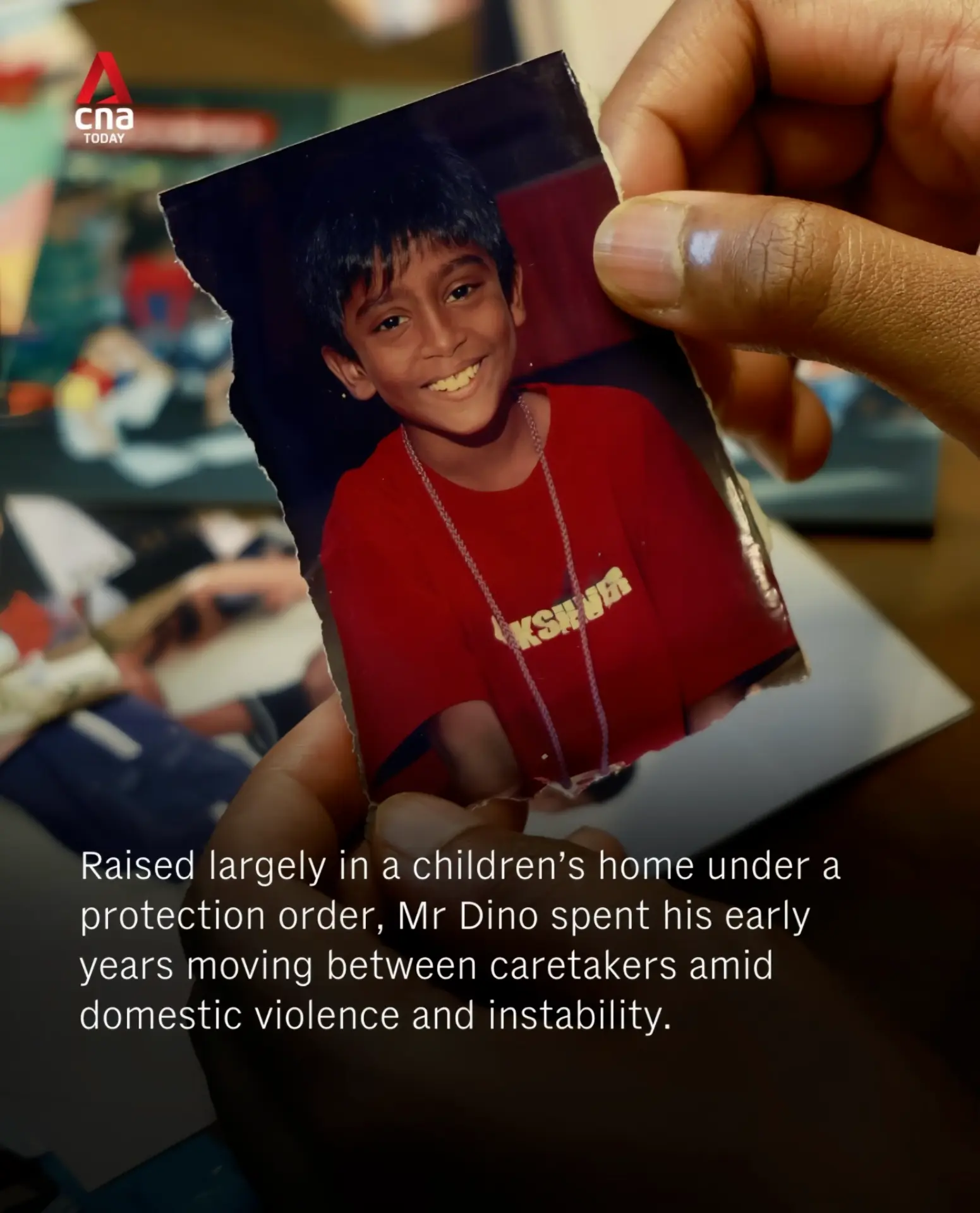 A hand holding a torn childhood photograph of a young Dino Isaac